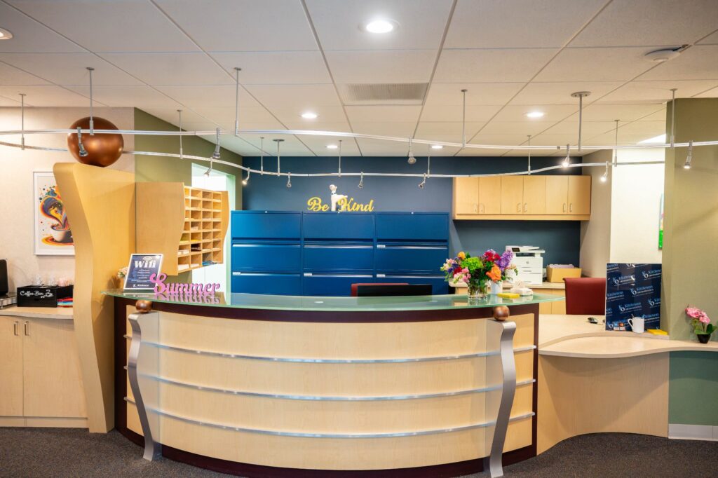 Modern orthodontic reception area at Kittleson Orthodontics in Mequon, featuring a welcoming front desk, colorful decor, and flowers, emphasizing a comfortable environment for patients seeking braces and orthodontic care.