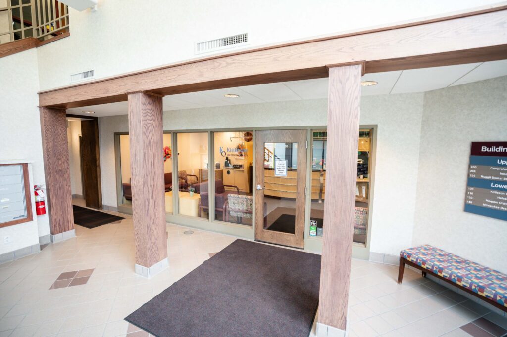 Modern entrance of Kittleson Orthodontics in Mequon, showcasing the welcoming reception area, with comfortable seating and a sign displaying office information and services related to orthodontics.