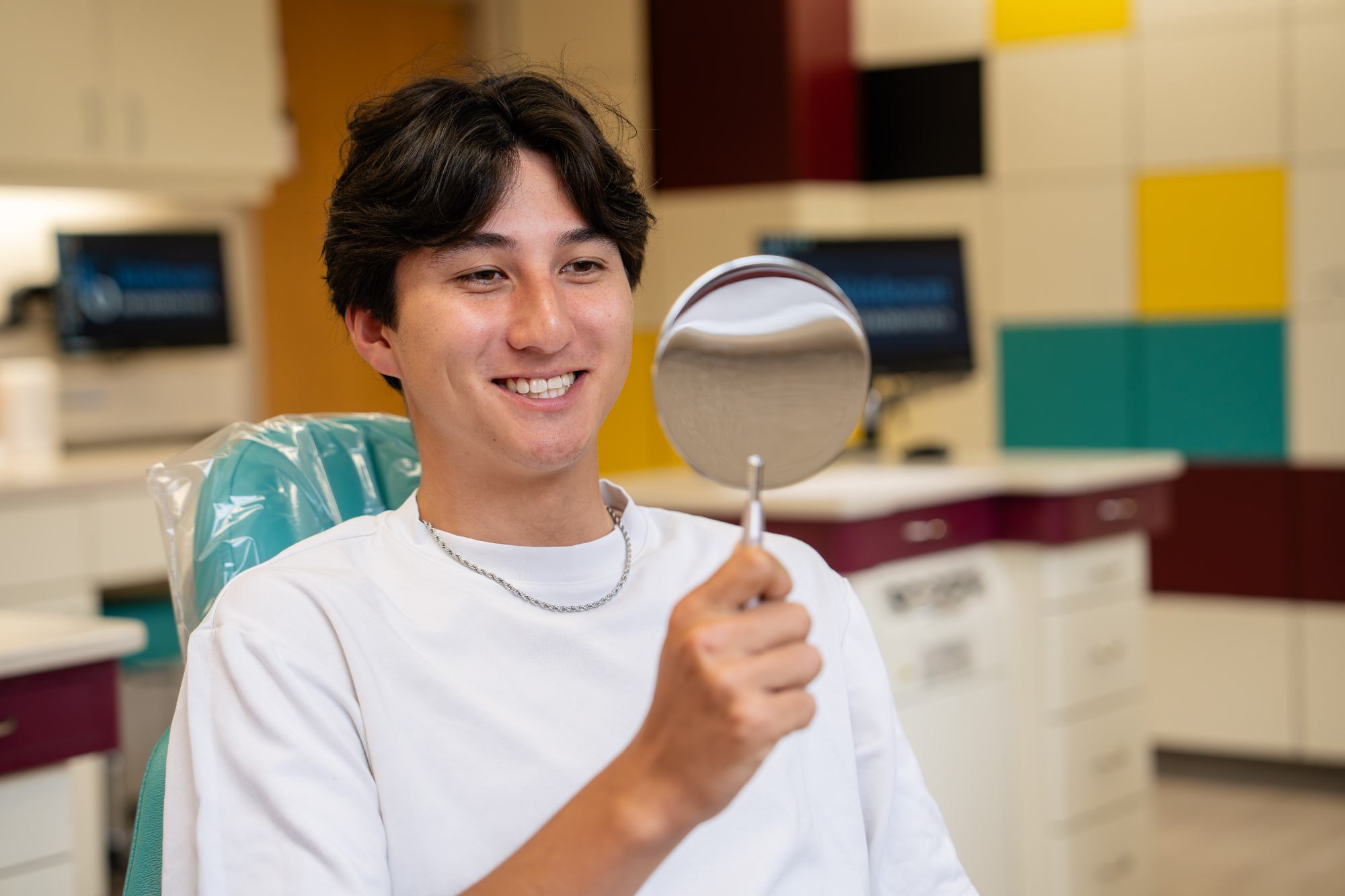 Teen smiling while holding a mirror in an orthodontic office, showcasing the positive experience of clear aligners at Kittleson Orthodontics in Mequon.