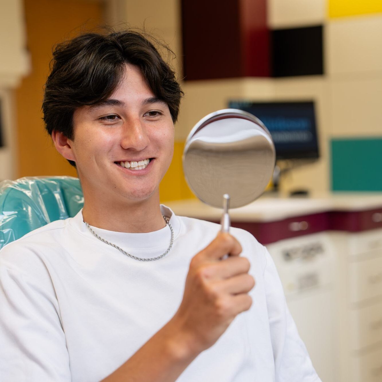 Smiling young patient holding a dental mirror in an orthodontic office, showcasing a positive experience at Kittleson Orthodontics in Mequon, highlighting braces treatment options.