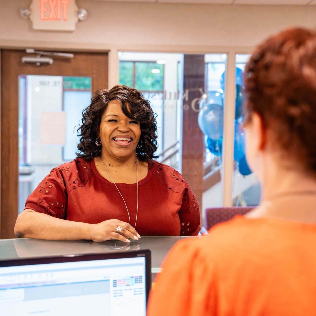Smiling woman at Kittleson Orthodontics reception desk engaging with staff, showcasing a welcoming atmosphere for Mequon orthodontic patients.